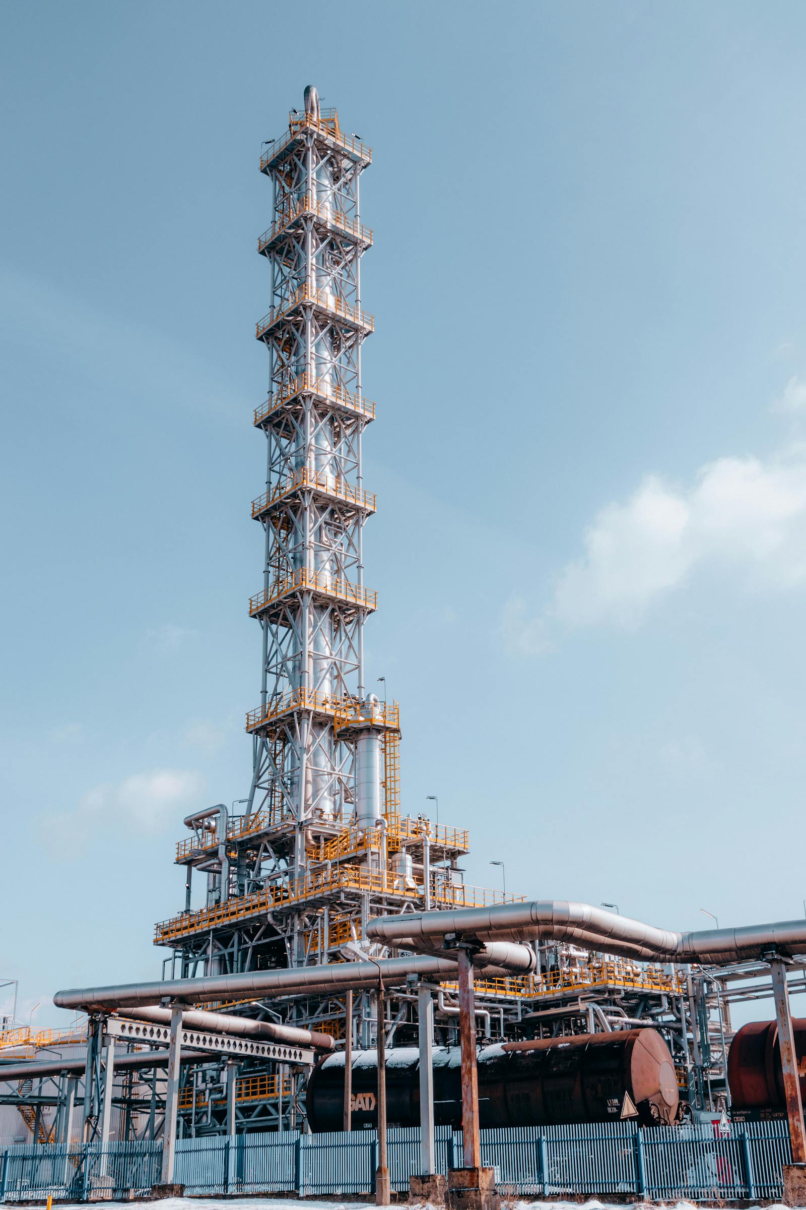 Wide shot of an oil and gas processing facility at dawn. Stack flare visible, pipework geometry in foreground.