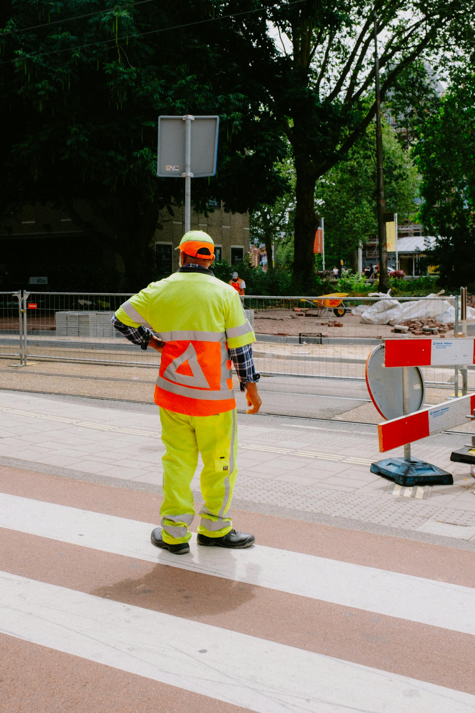 Wide shot of an active construction site with workers in hi-vis vests and helmets. Crane silhouette and scaffolding visible in background.