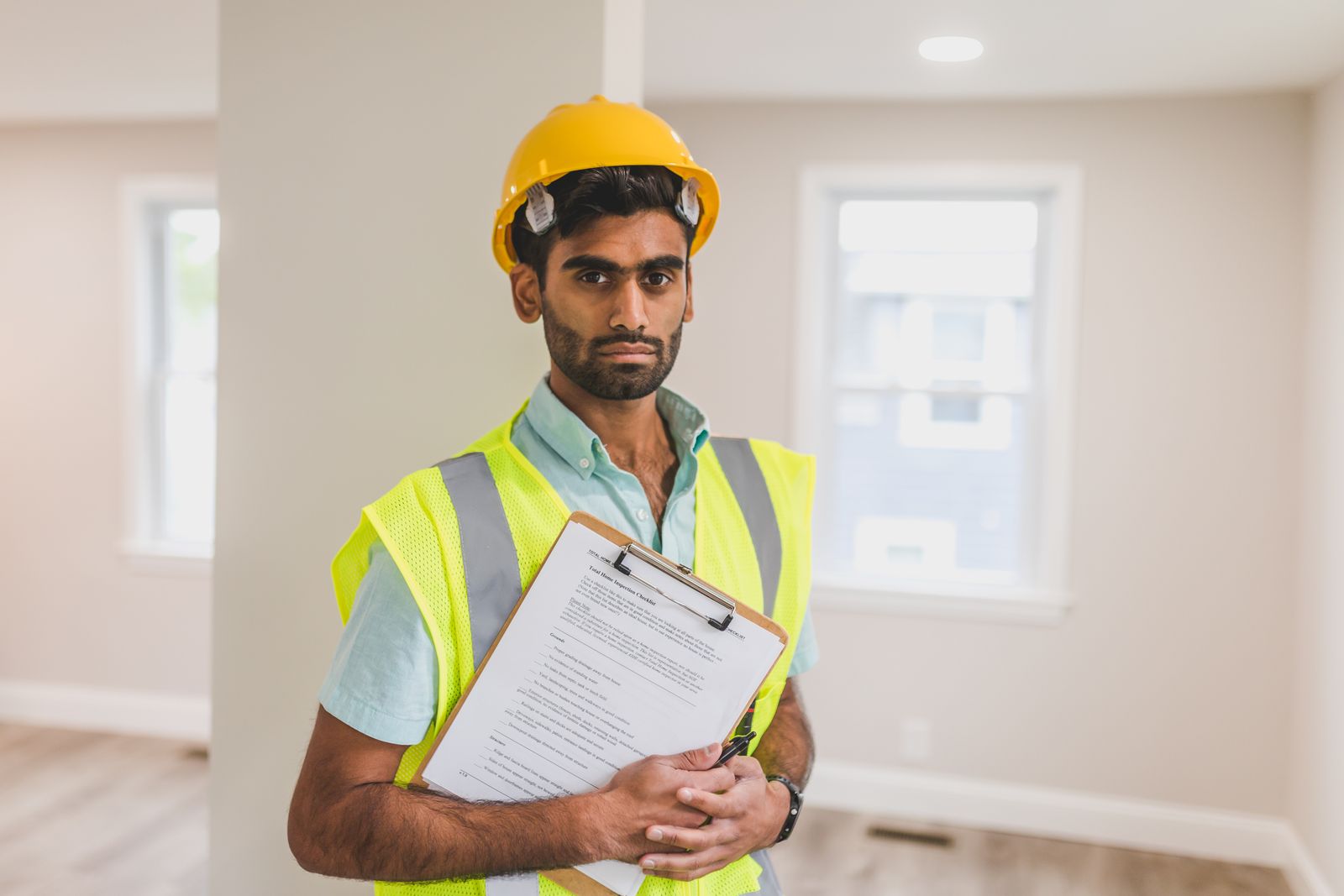 An EHS auditor walking a manufacturing floor with a tablet, checking items against equipment while an operator looks on, both in hi-vis vests.