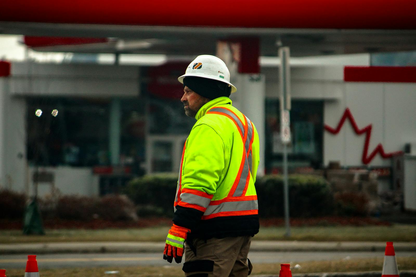 Worker on industrial floor speaking into a phone to file a safety observation. Hands and device in focus, hi-vis vest visible.